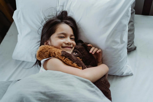Smiling child in bed cuddling a plush toy, bedtime comfort for kids, clean bedding