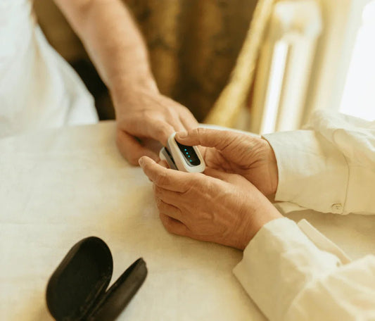 Person using a portable pulse oximeter on another's finger at a home table