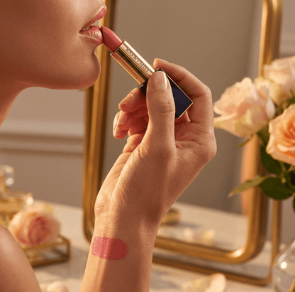 Person applying lipstick with a mirror and flowers in the background