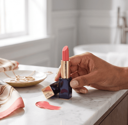 Hand holding a pink lipstick on a marble surface with a blurred background