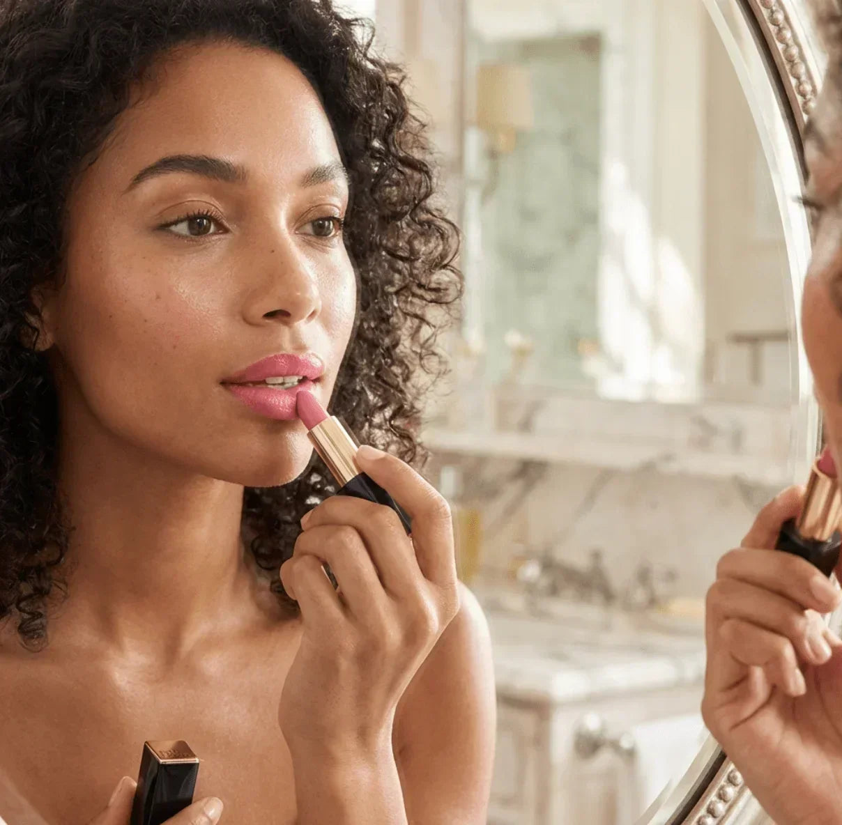 Woman applying pink lipstick in front of bathroom mirror for natural makeup look