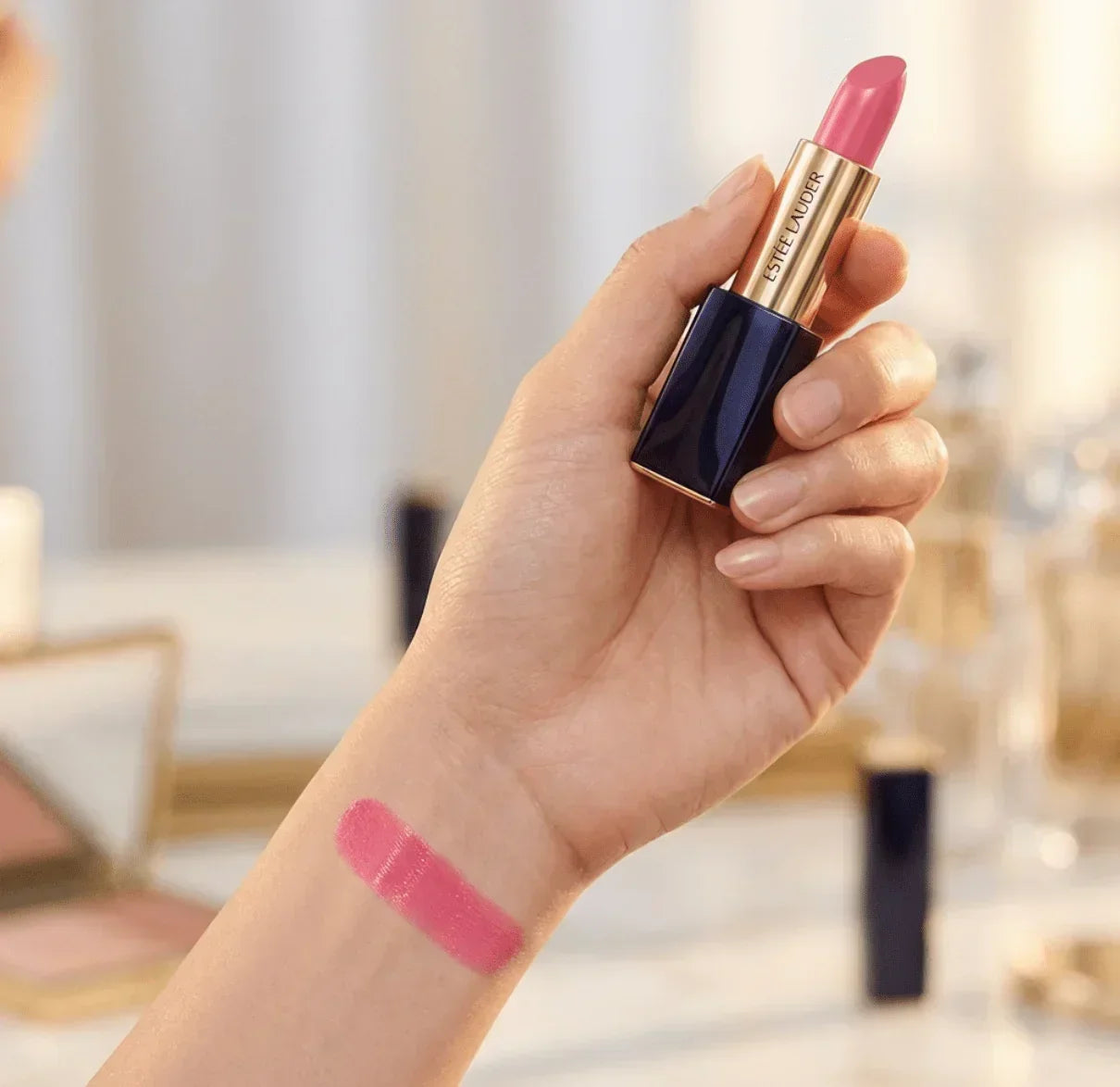 Hand holding pink lipstick with pink lipstick swatch on wrist, beauty makeup product