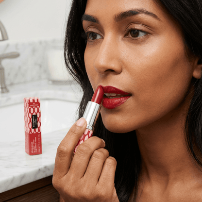 Woman applying red lipstick with a visible lipstick tube in the background