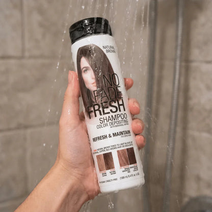 Hand holding No Fade Fresh color depositing shampoo bottle under shower water